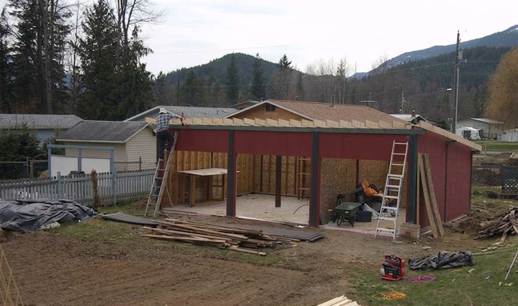 Building under construction in a rural area with mountains and trees in the background, people working on the roof