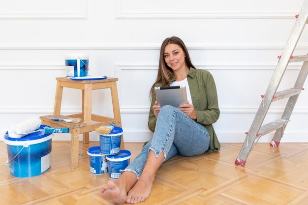 woman sitting on the floor surrounded by paint cans and a ladder, preparing for a painting project